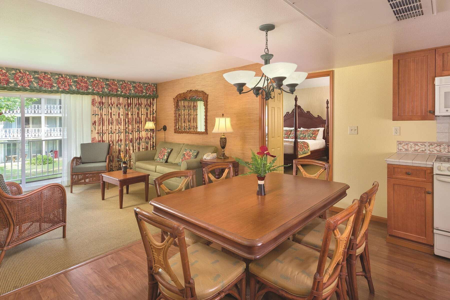 A dining area with a wooden table and chairs, a sofa, a lamp, and a view of the outside.