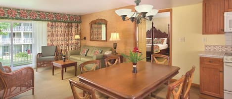 A dining area with a wooden table and chairs, a sofa, a lamp, and a view of the outside.