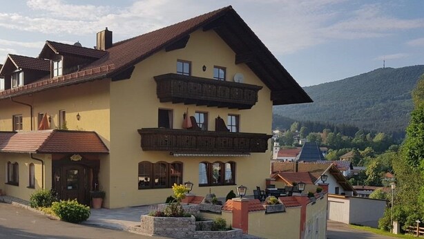 En toetages bygning med balkon, et skilt der angiver at det er en restaurant, og udsigt til et bjerg i baggrunden.