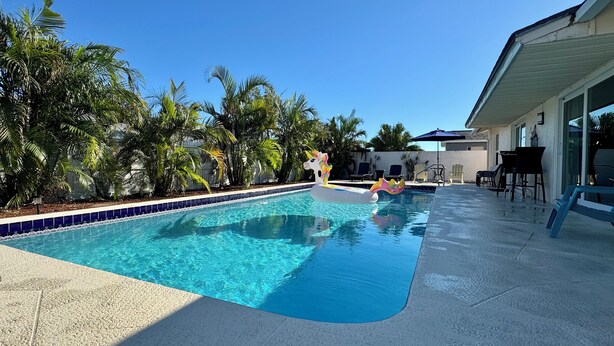 Ein Swimmingpool mit einem Einhorn-Schwimmtier, umgeben von Palmen und Gartenmöbeln.