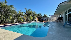 Una piscina con un flotador de unicornio, rodeada de palmeras y mobiliario de exterior.