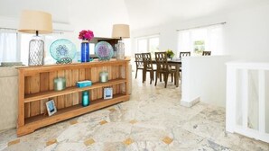 Ein geräumiger Raum mit einem Holzbodenregal, das dekorative Gegenstände beherbergt, einem Essbereich mit Tisch und Stühlen sowie einem Deckenventilator.