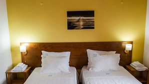 Une chambre d’hôtel avec deux lits simples, chacun doté d’une tête de lit en bois, de draps blancs et d’une petite table de chevet avec une lampe.