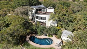Una casa moderna con una piscina curvada, rodeada de abundante vegetación.