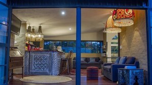 Una sala moderna con un sofá, un reposapiés y una mesa de centro. Hay una zona de cocina con barra y lámparas colgantes.