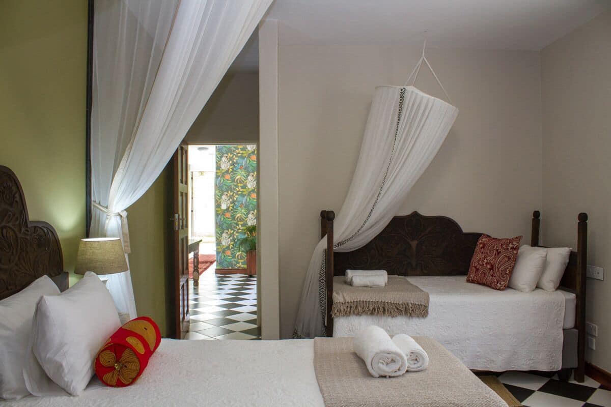 A hotel room with two beds, one with a canopy, and a checkered floor.