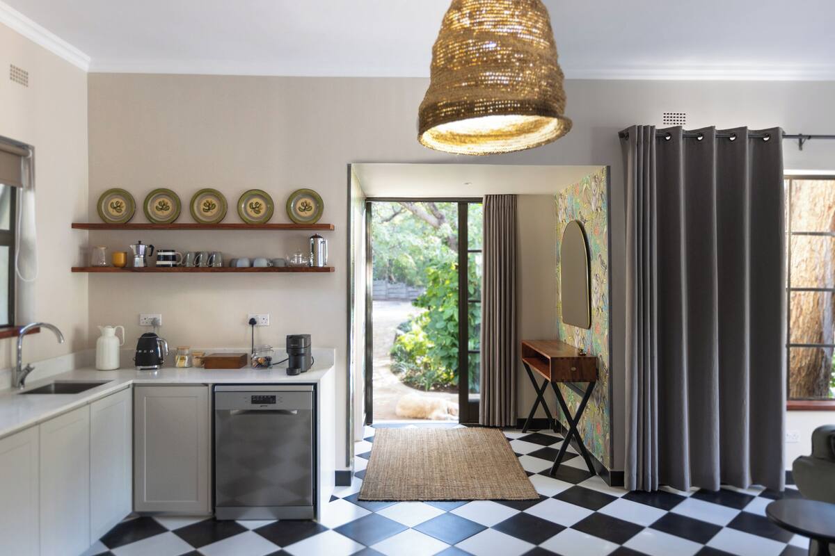 A modern kitchen with a dishwasher, a coffee maker, and a small dining area with a table and chair.