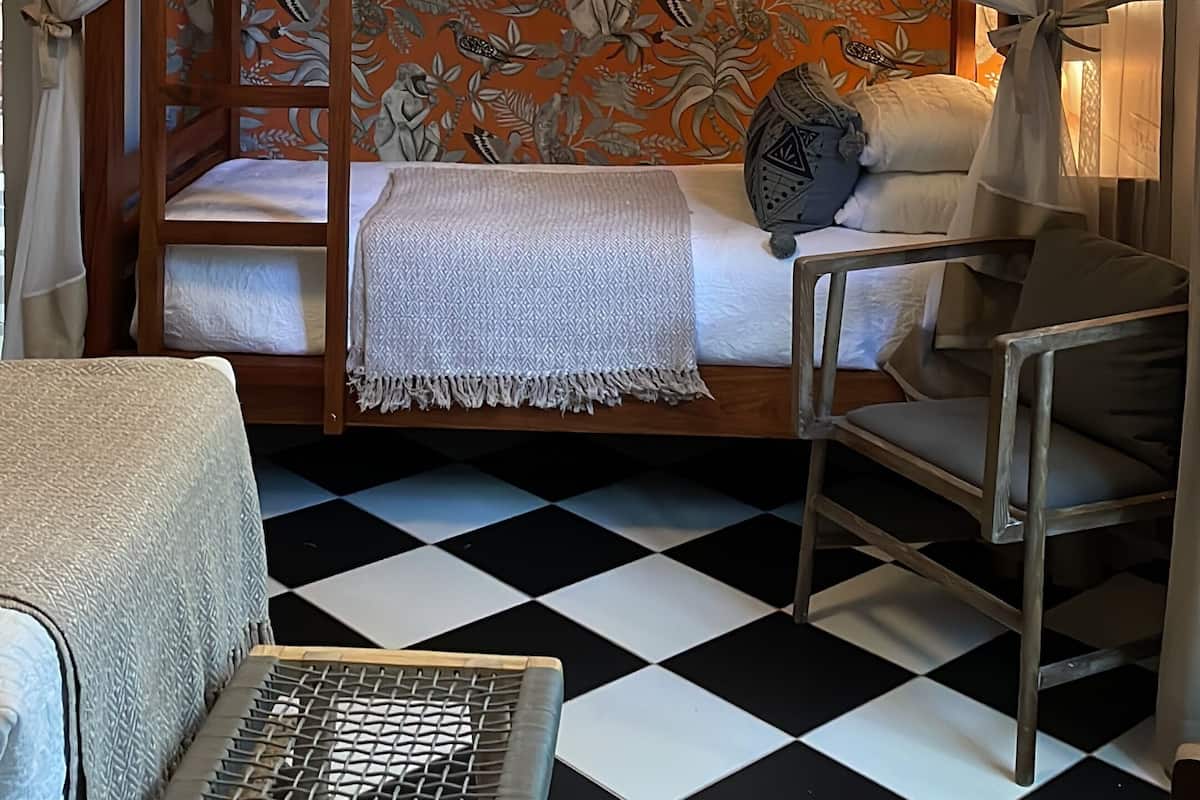 A room with a bed under a canopy, a chair, and a checkered floor.