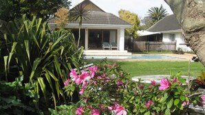 A house with a covered patio, a swimming pool, and lush greenery. - Wilmot Cottages (Gqeberha (Port Elizabeth))