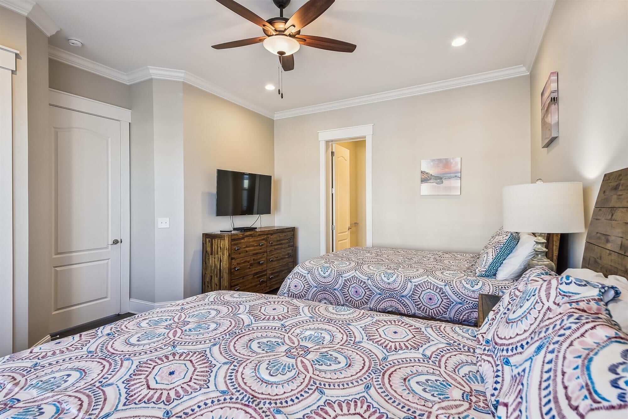 A bedroom with two beds, a ceiling fan, a television, and a door leading to another room.