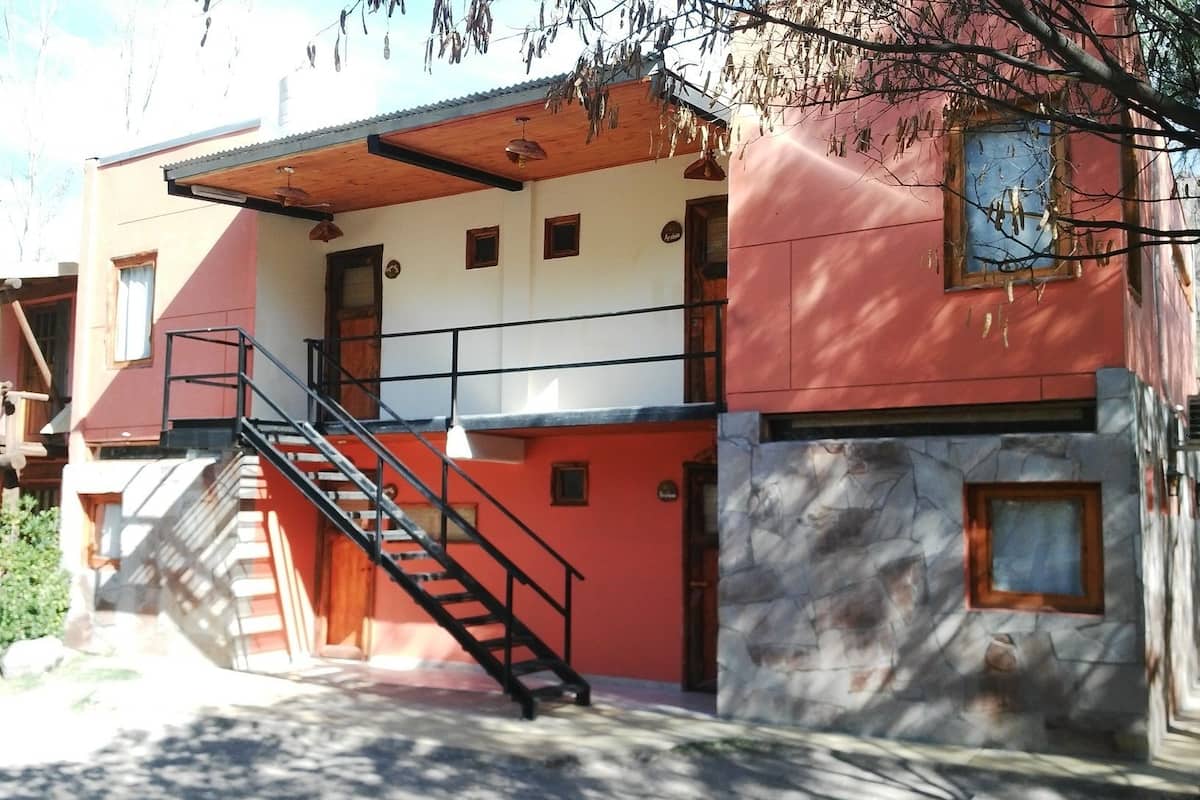Un edificio con fachada roja y blanca, un muro de piedra y una escalera que conduce a un nivel superior.