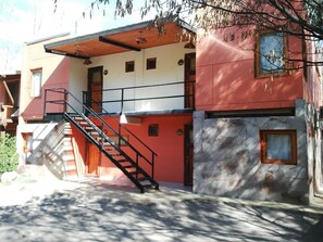 A building with a red and white facade, a stone wall, and a staircase leading to an upper level. - Cabañas Rocas Amarillas (El Nihuil)
