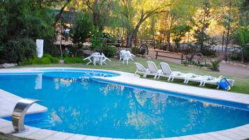 A swimming pool with white lounge chairs and a wooden bench.