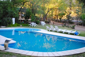 A swimming pool with white lounge chairs and a wooden bench. - Cabañas Rocas Amarillas (El Nihuil)