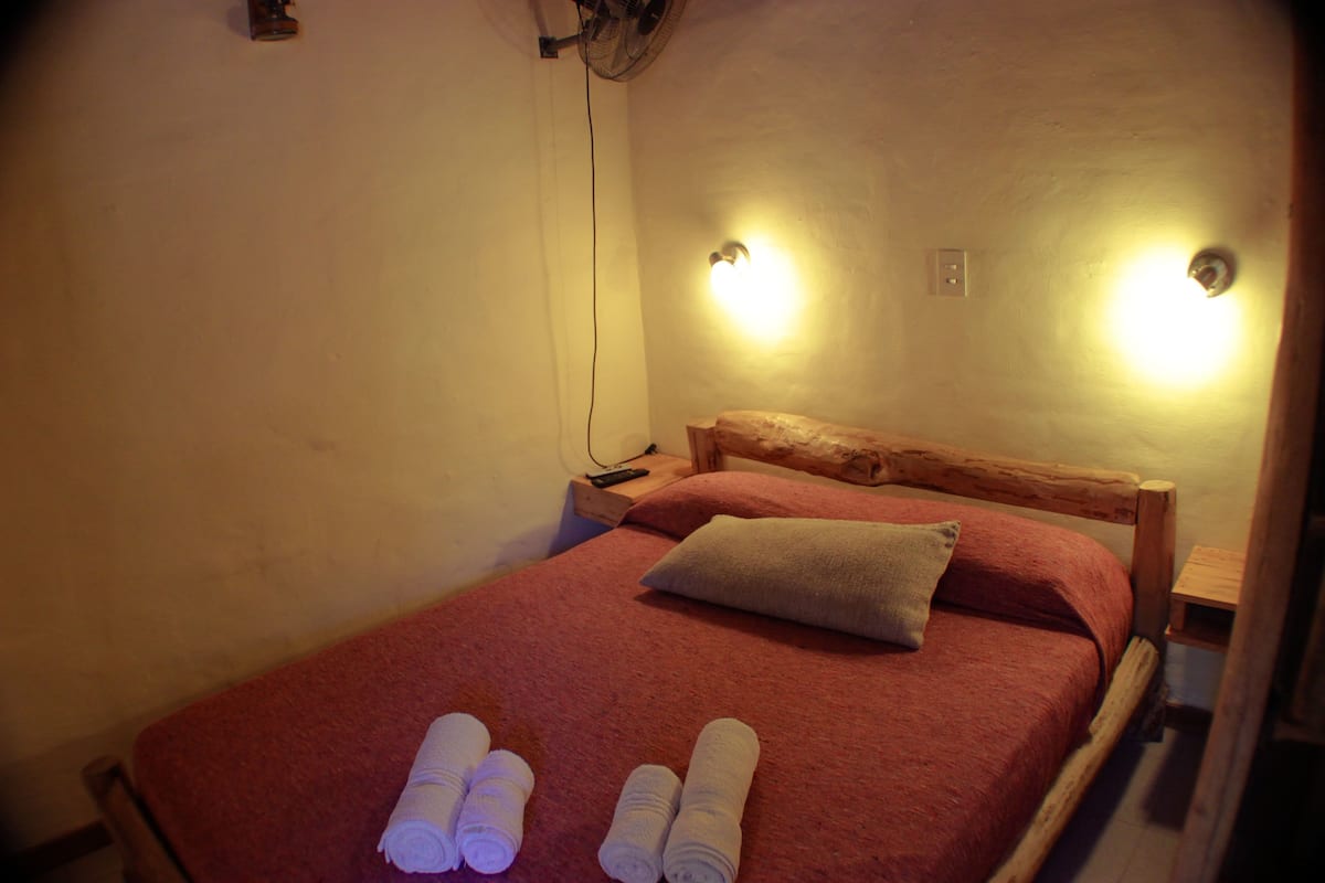 Una habitación pequeña y acogedora con una cama individual, un cabecero de madera y dos lámparas fijadas a la pared.