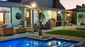 A modern house with a swimming pool, outdoor seating, and a covered patio area.