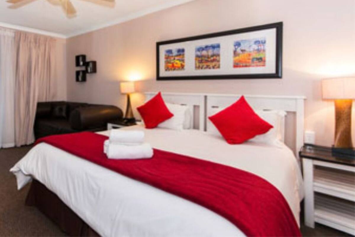 Habitación de hotel con cama, escritorio, silla, ventilador de techo y obras de arte en la pared.