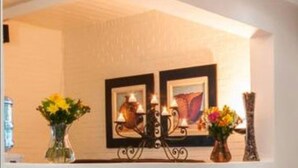 A room with a white brick wall, a candelabra with candles, and two framed artworks.