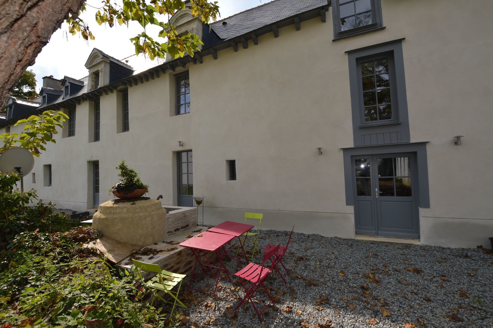 Ein Gebäude mit weißer Fassade, mehreren Fenstern und einer Tür. Eine Terrasse mit Tisch und Stühlen sowie einem Blumentopf.