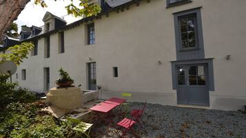 Ein Gebäude mit weißer Fassade, mehreren Fenstern und einer Tür. Eine Terrasse mit Tisch und Stühlen sowie einem Blumentopf.