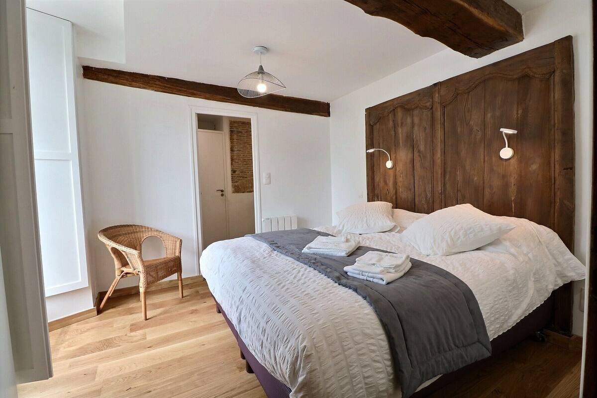 A bedroom with a bed, a chair, a wooden headboard, and a hanging light fixture.