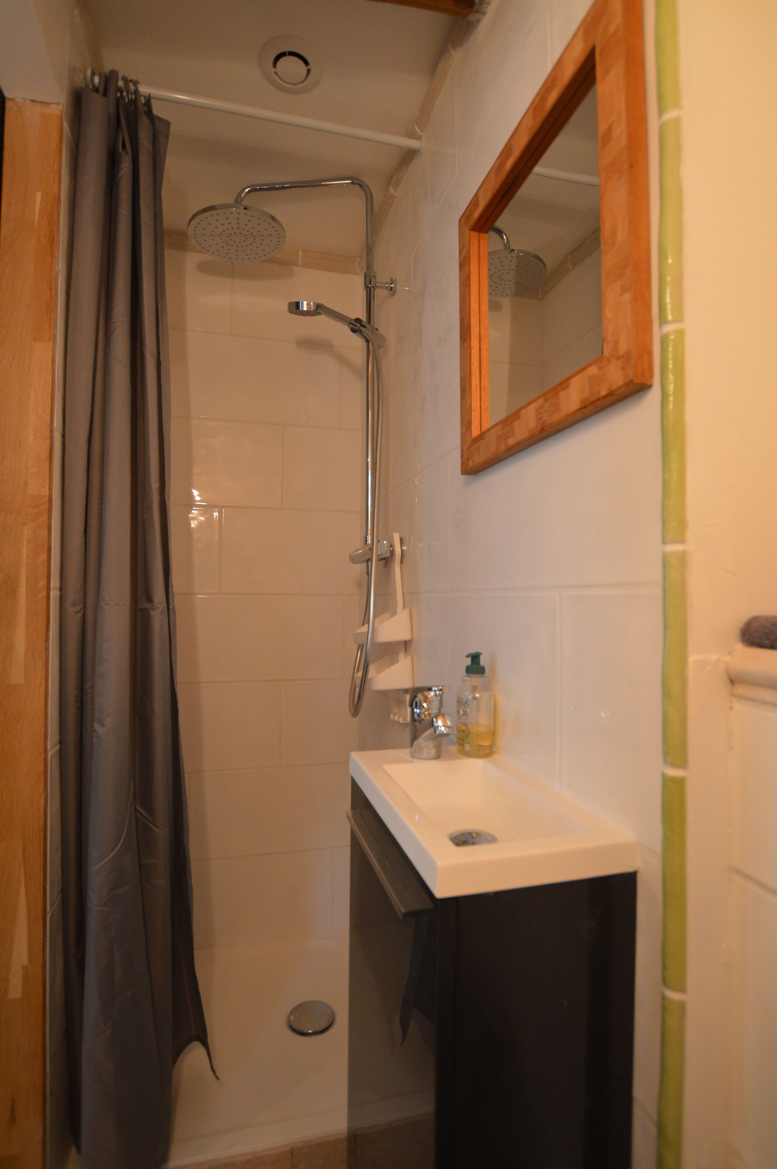 Una ducha con cabezal de ducha manual, un lavabo con protección de vidrio y un espejo sobre él.