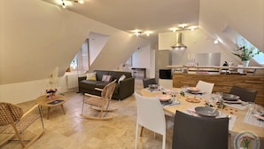 Amplia sala de estar con una mesa de comedor preparada para cuatro, un sofá y una cocina al fondo.