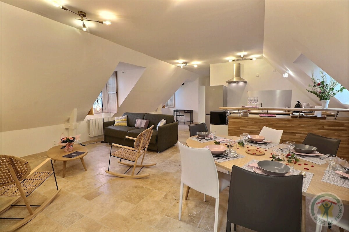 A spacious living area with a dining table set for four, a sofa, and a kitchen in the background.