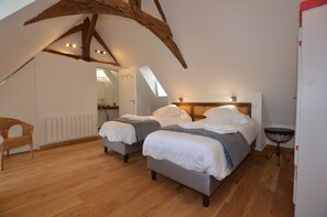 A bedroom with two beds, wooden floors, a sloped ceiling, and a small table. - Chateau des Fontenelles (Chavagne)