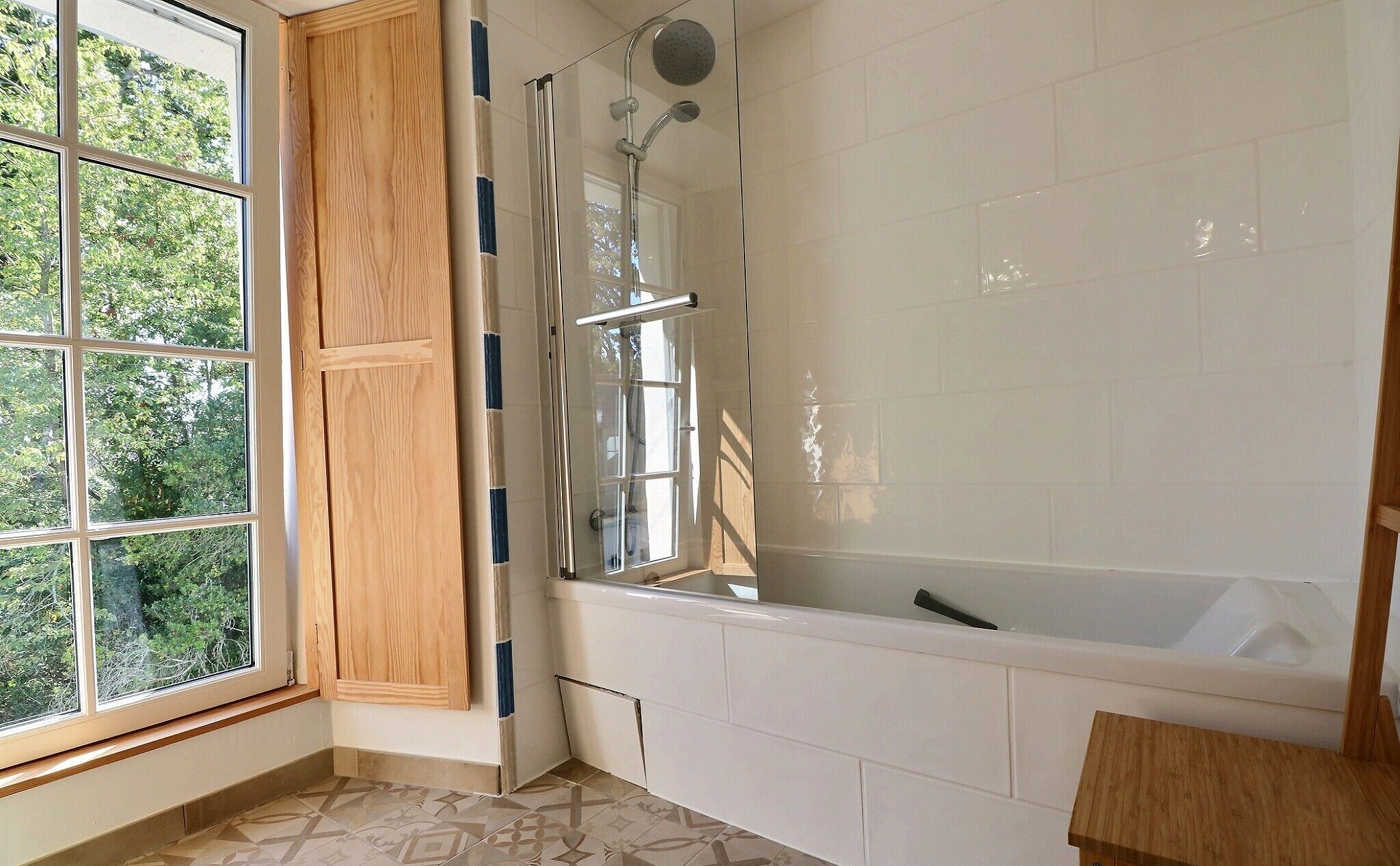 A bathroom with a bathtub, a shower, and a window with wooden shutters.