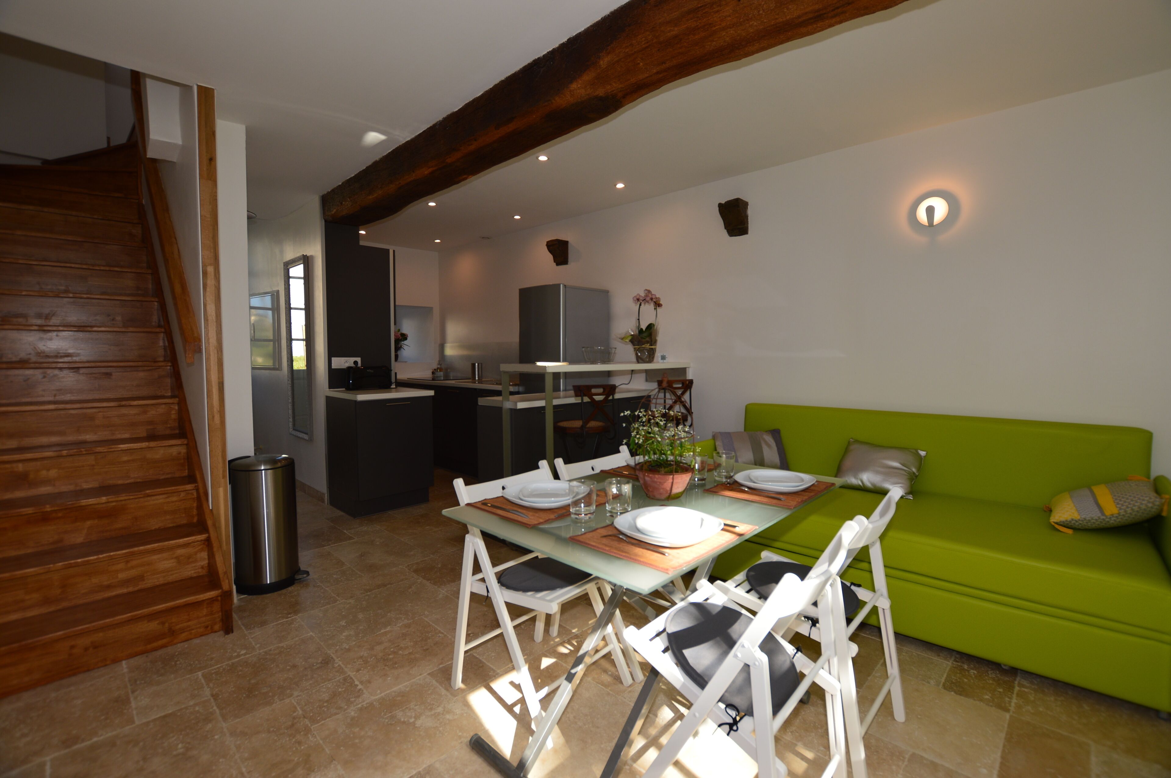 A dining area with a table set for four, a green sofa, and a kitchen in the background.