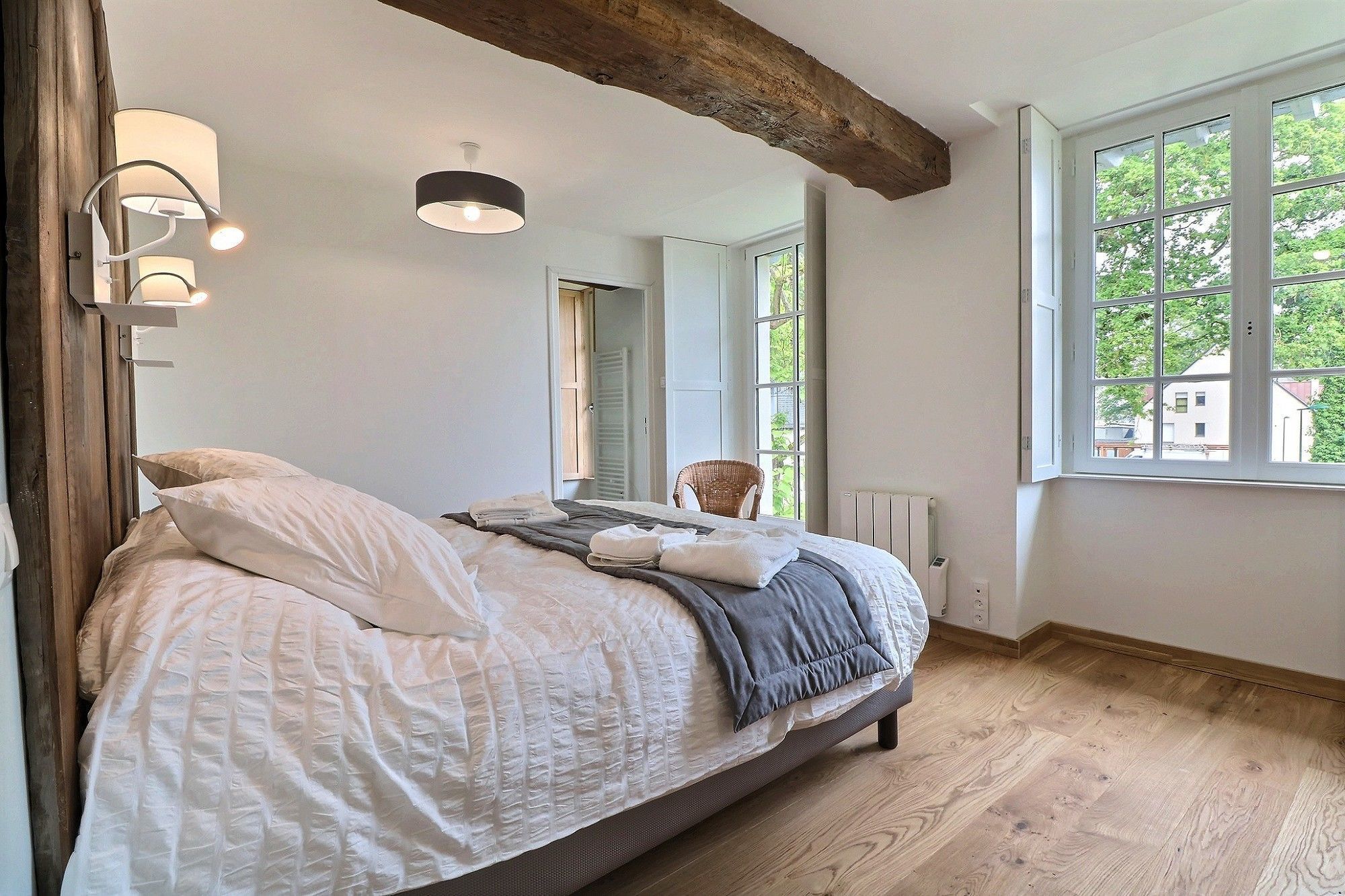 Een slaapkamer met een groot bed, houten balken, een raam met uitzicht en wandlampen.