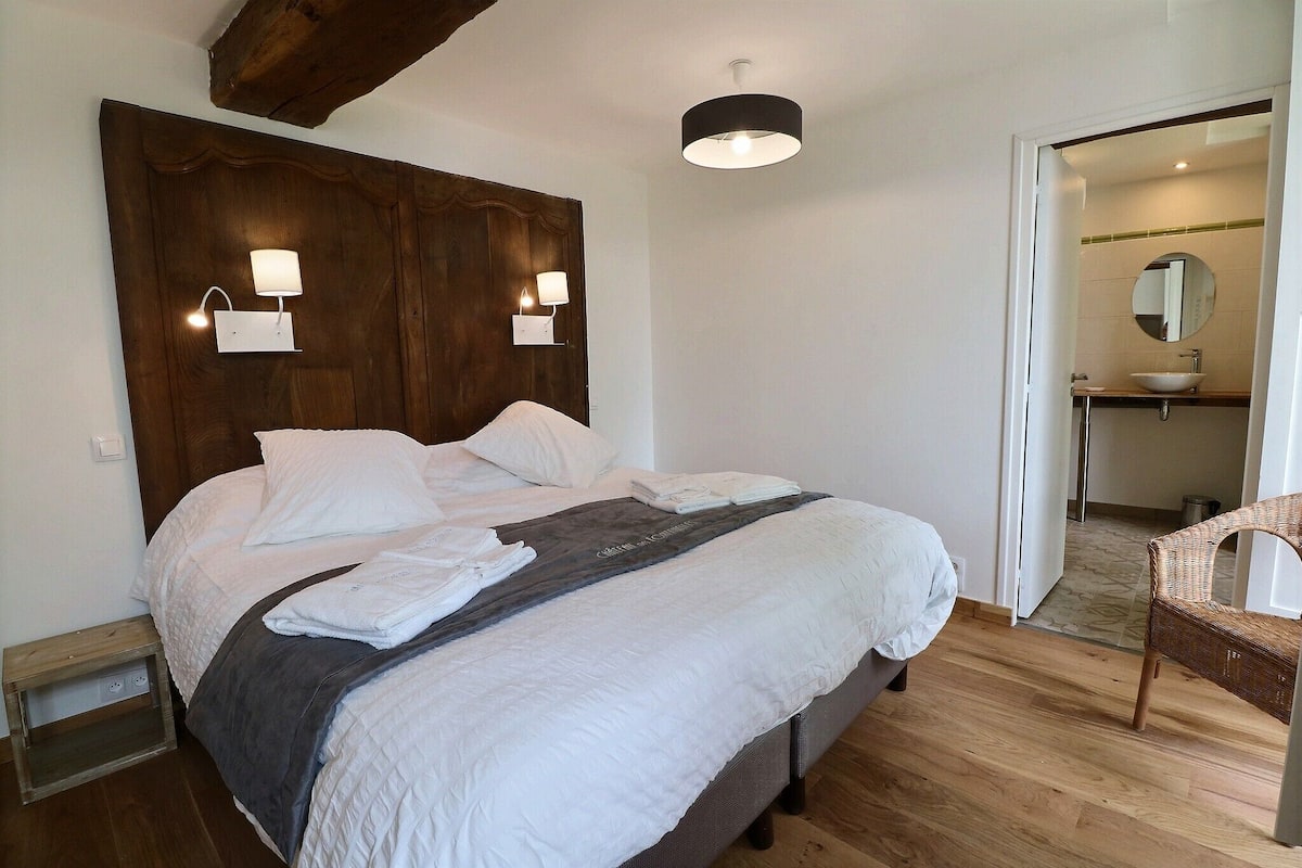 A bedroom with a large bed, two wall-mounted lights, a wooden headboard, and a visible bathroom with a sink and mirror.