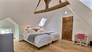 Un dormitorio con techo inclinado, una puerta de madera, un escritorio con silla, y una cama con almohadas y manta.