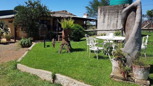 A grassy outdoor area with a table and chairs, a water tank, and a building in the background. - The Hay Barn (Lions River)