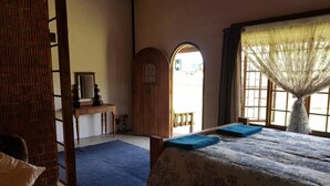 A room with a bed, a wooden bench, a small table with a mirror, and a door leading outside. - The Hay Barn (Lions River)