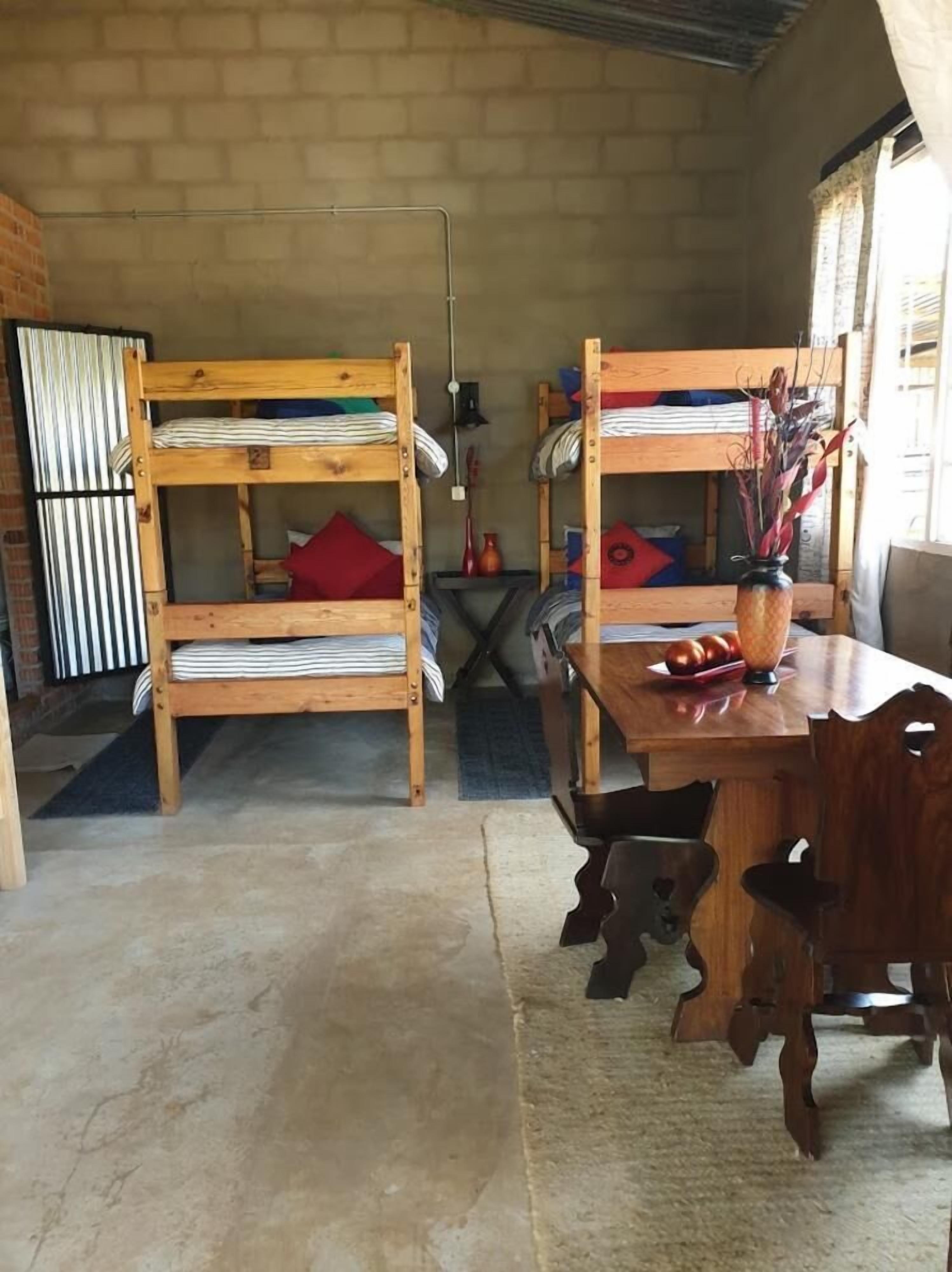 Una habitación rústica con dos literas, una mesa de madera con un florero y una pared de ladrillo.