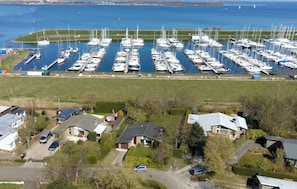 An aerial view of a marina with numerous boats docked, surrounded by residential houses and a grassy field. - Detached house with 750 sqm of land on the North Sea and Grevelingen sea (Scharendijke)