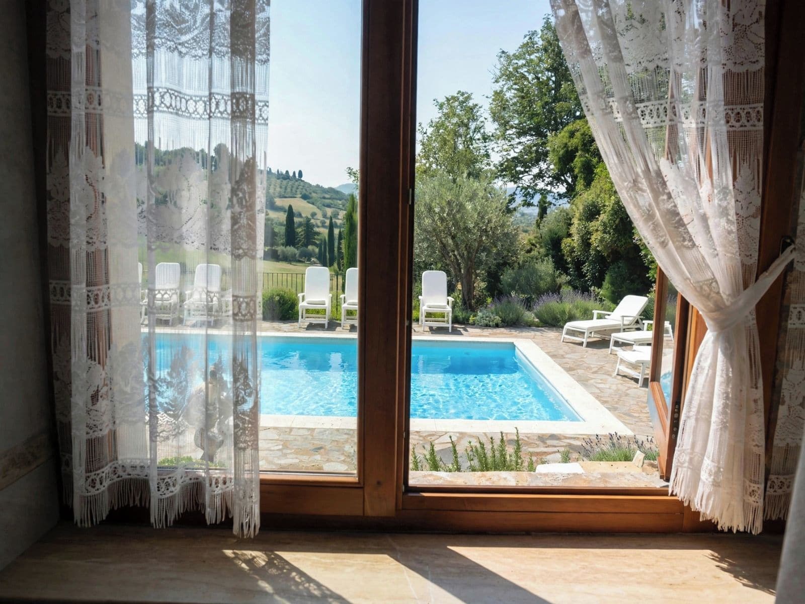 A room with a view of a swimming pool, white curtains, and a wooden floor.