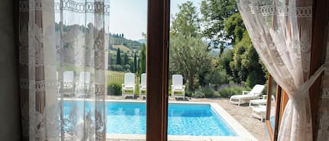 A room with a view of a swimming pool, white curtains, and a wooden floor.