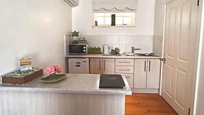 A compact kitchen with white cabinets, a microwave, a kettle, and a small countertop with a book and a vase of flowers. - On The Bay B&B (Gqeberha (Port Elizabeth))
