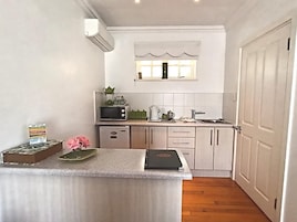 A compact kitchen with white cabinets, a microwave, a kettle, and a small countertop with a book and a vase of flowers.