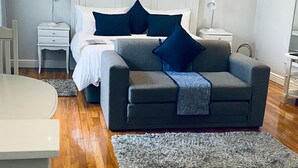 A modern living room with a grey sofa, a white headboard, and a ceiling fan. - On The Bay B&B (Gqeberha (Port Elizabeth))