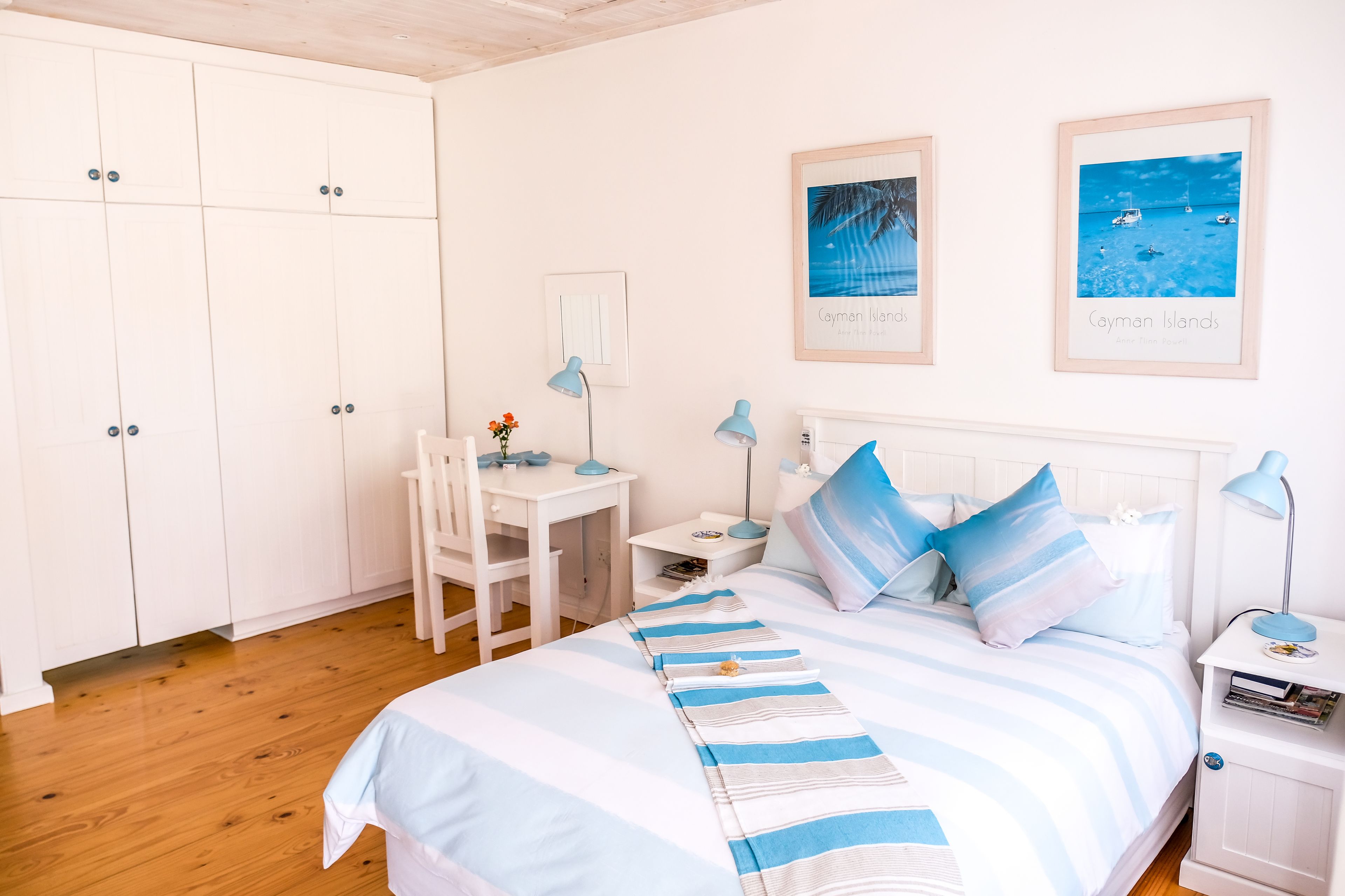 A bedroom with a bed, a desk, a chair, and a wardrobe. There are two framed pictures on the wall.