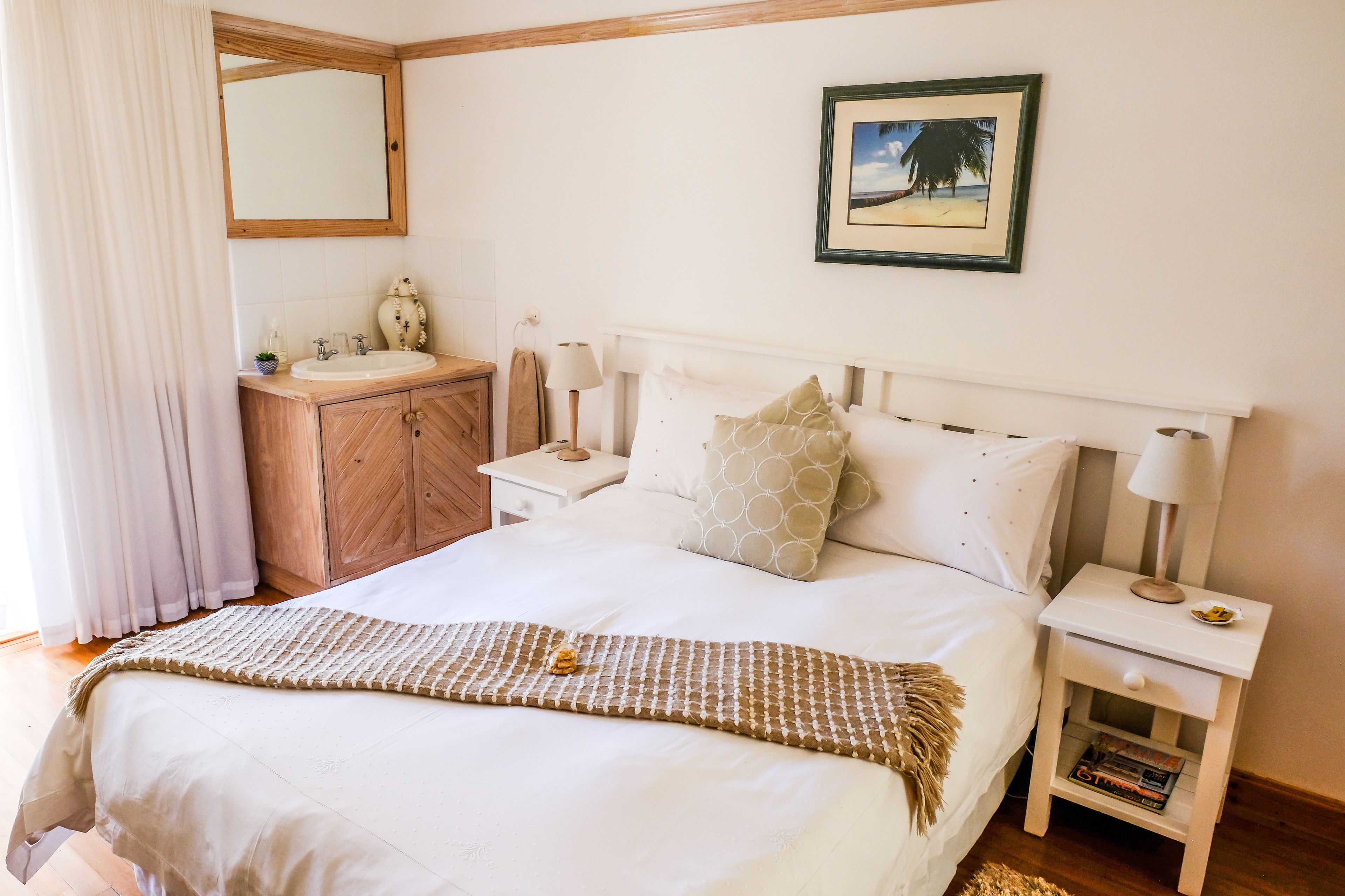 A neatly arranged bedroom with a bed, bedside tables, a vanity with a mirror, and a framed picture on the wall.