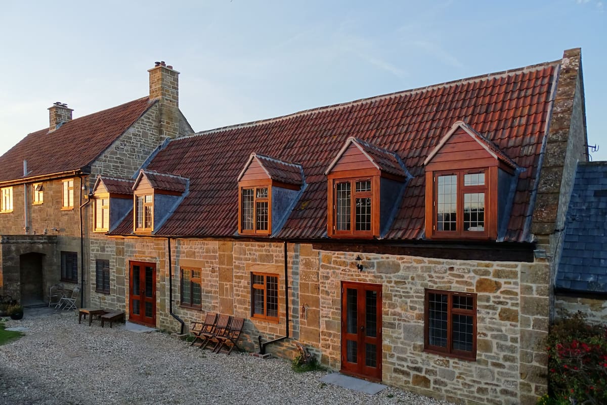 A stone building with a red-tiled roof, multiple windows, and a gravel driveway.