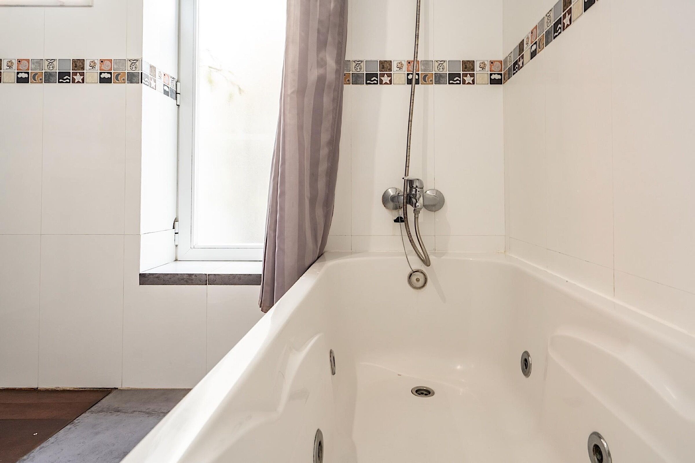 A bathroom with a bathtub, a shower, and a window with curtains.