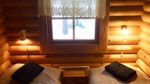 A log cabin room with two beds, a window with lace curtains, and two wall-mounted lamps. - Villa Luppopirtti (Sodankyla)