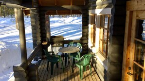 A wooden deck with a table and chairs, overlooking a snowy landscape. - Villa Luppopirtti (Sodankyla)