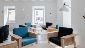 Un área de descanso moderna y bien iluminada, con mobiliario de madera, cojines azules y negros, y un suelo con estampado geométrico.